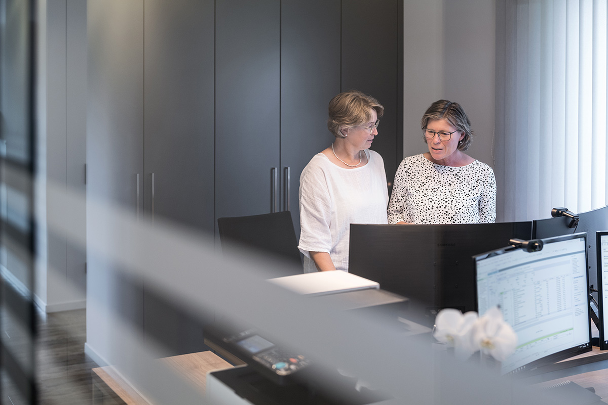 Zwei Mitarbeiterinen beim Gespräch am Schreibtisch in einem Büro mit Glaswand