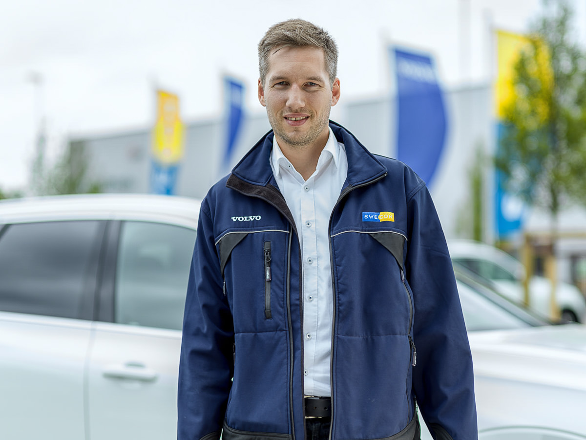 Portrait KFZ Verkäufer vor Unternehmensfahnen.