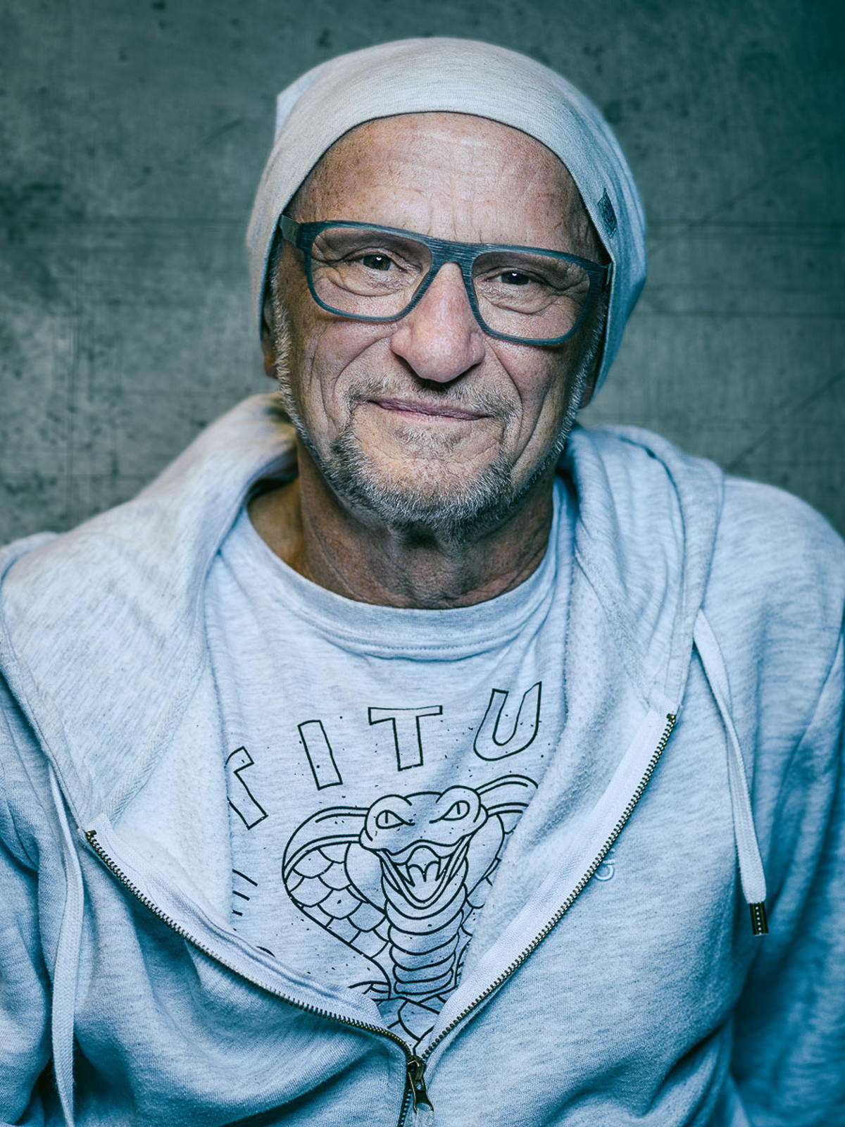 Person in grauem Hoodie und T-Shirt mit Schlangenmotiv vor grauem Hintergrund, einzigartiges Design.