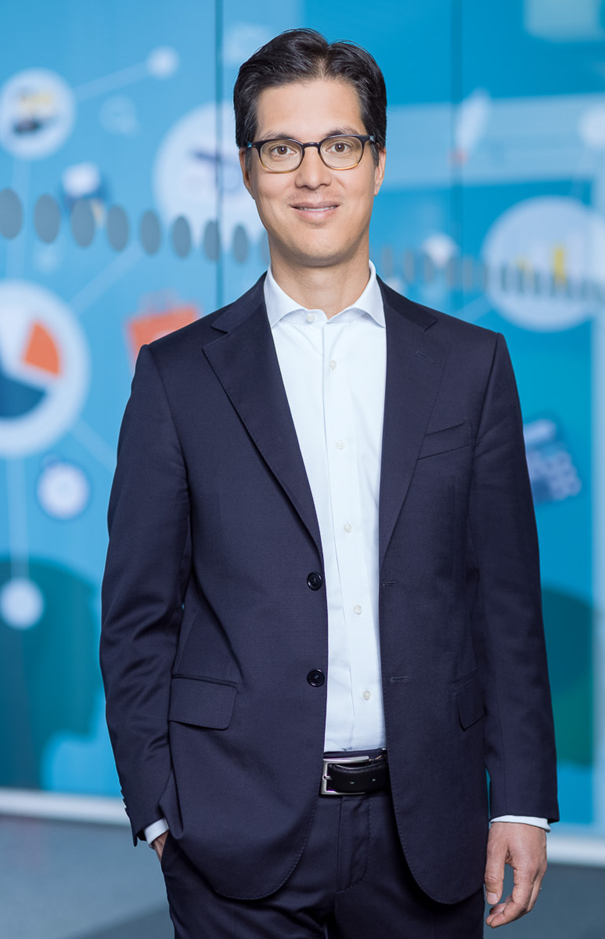 Mann in Anzug und Brille posiert vor einer blauen Wand. 