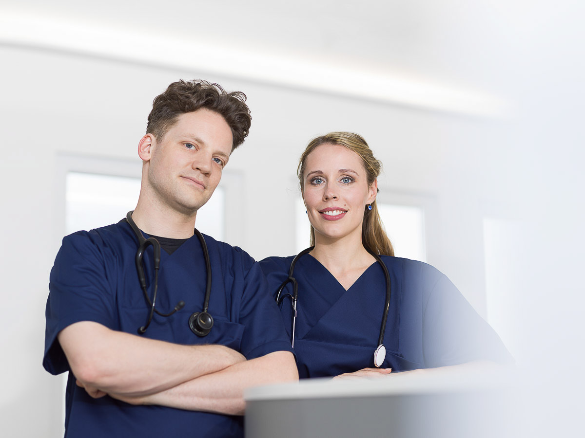 Ein Mann und eine Frau in medizinischen Kitteln, die in einem MVZ arbeiten und freundlich miteinander sprechen.