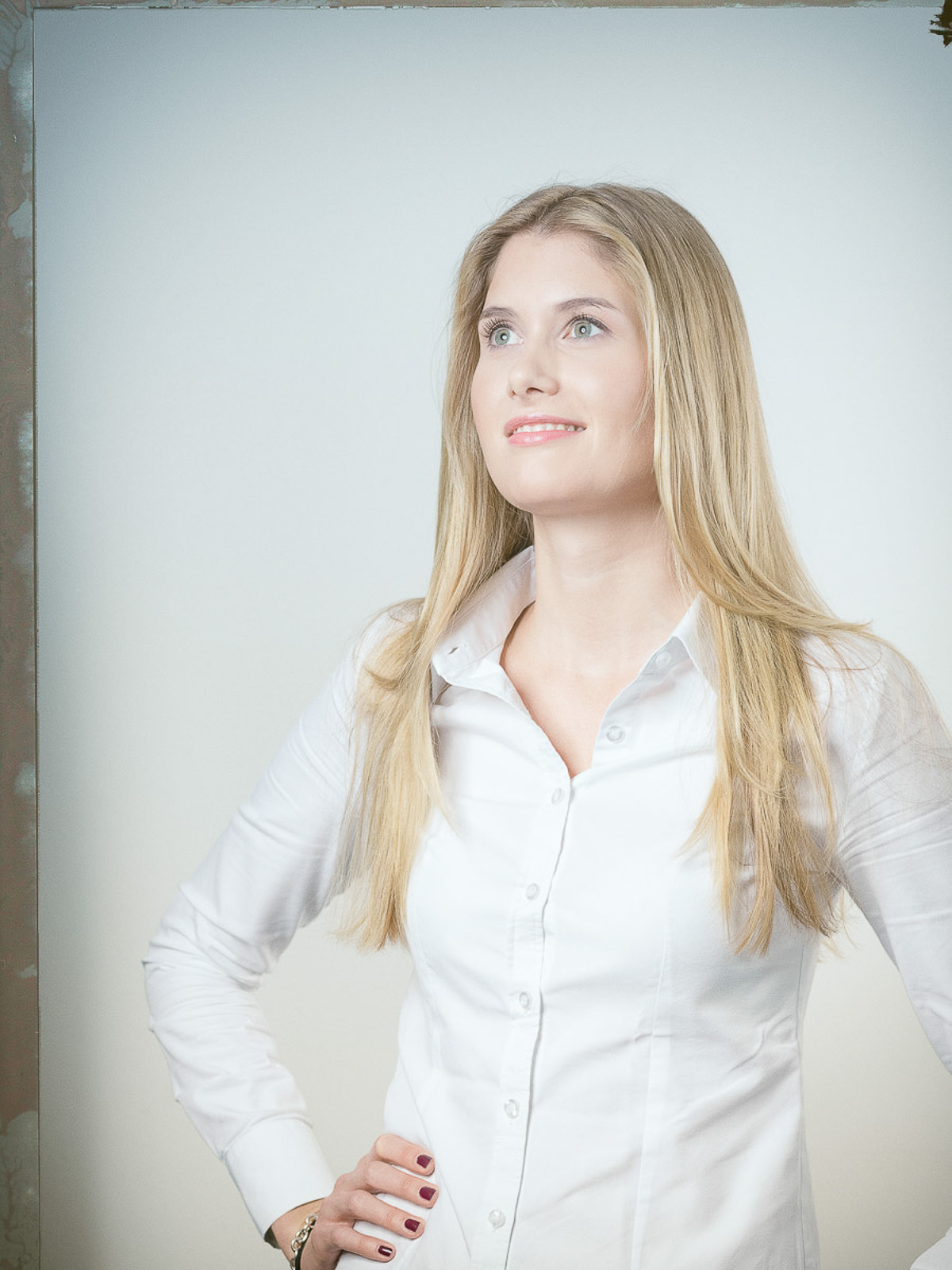Junge Frau mit langen blonden Haaren in weißer Bluse, strahlender Blick. Business-Porträt mit natürlichem Licht und sanften Farben.