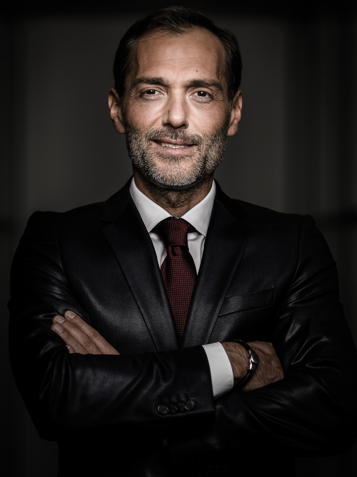 Kampagnenportrait mit einem Geschäftsmann im dunklen Anzug, fotografiert in einem sehr dunklen Raum mit Fokus auf sein Gesicht.