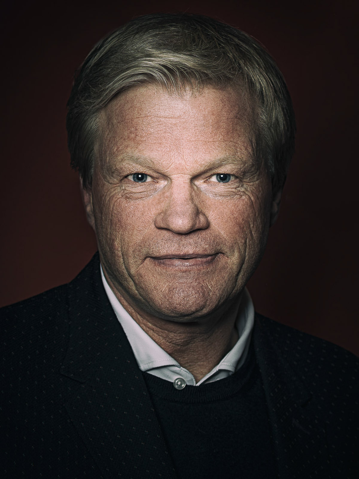 Oliver Kahn im Porträt, dunklen Anzug mit weißem Hemd vor dunklem Hintergrund, formell und professionell.