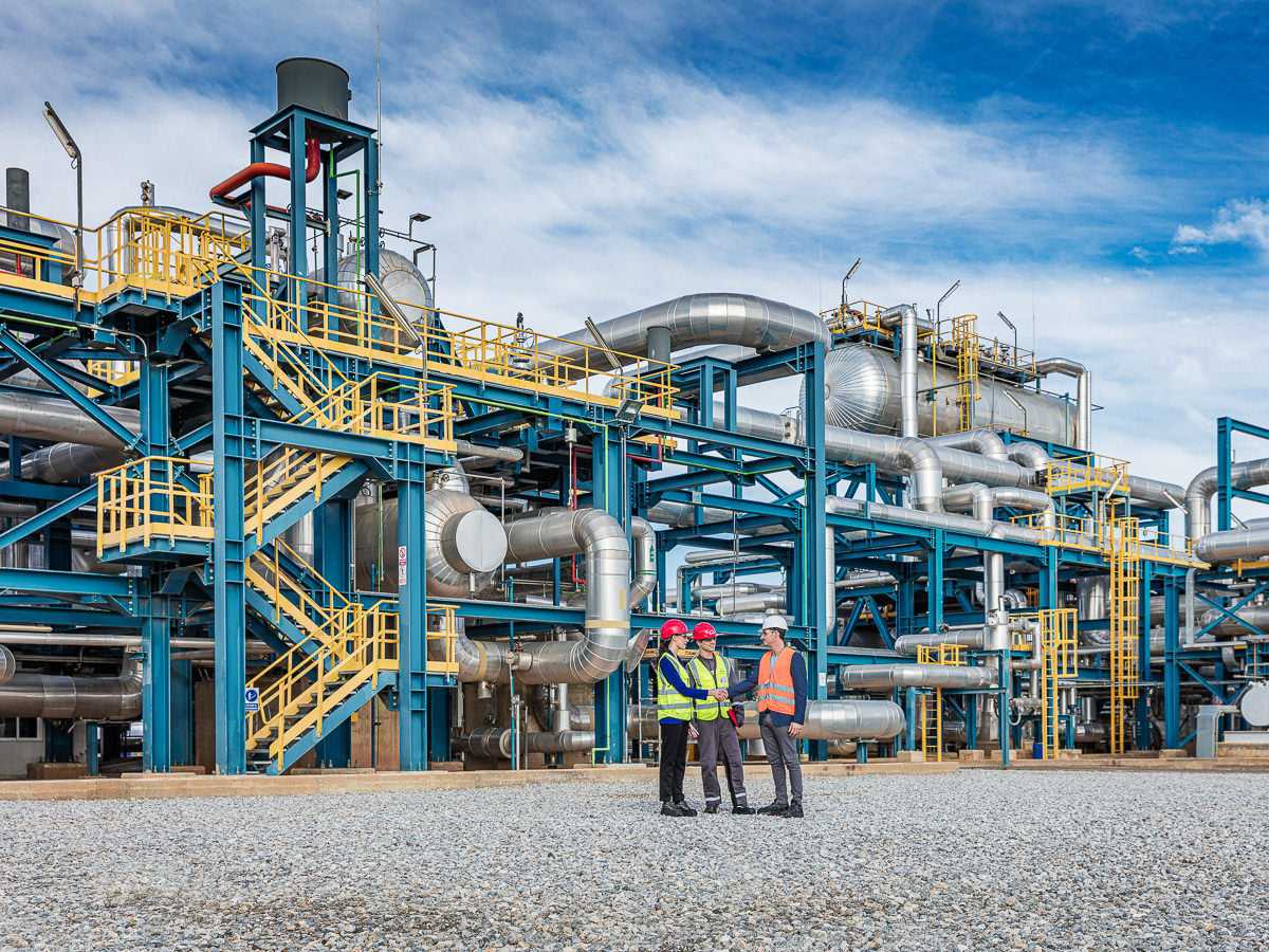 Gespräch von Ingeneur, Mitarbeiter und Kunde vor Industrieanlage im Freien.